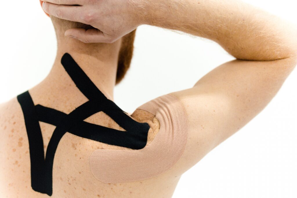 A man with kinesiology tape applied on his shoulder against a white background, showcasing physical therapy support.